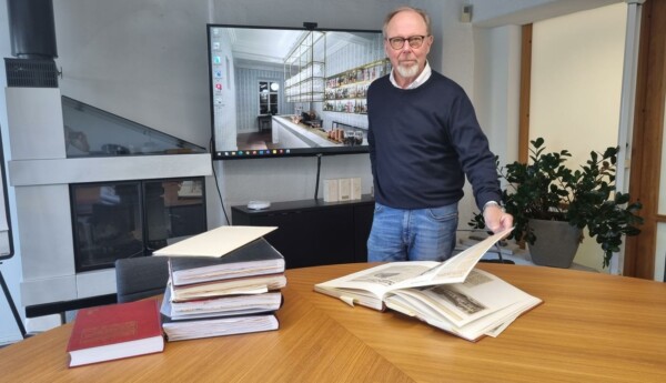 man står vid bord och bläddrar i tjocka liggare med tidningsurklipp