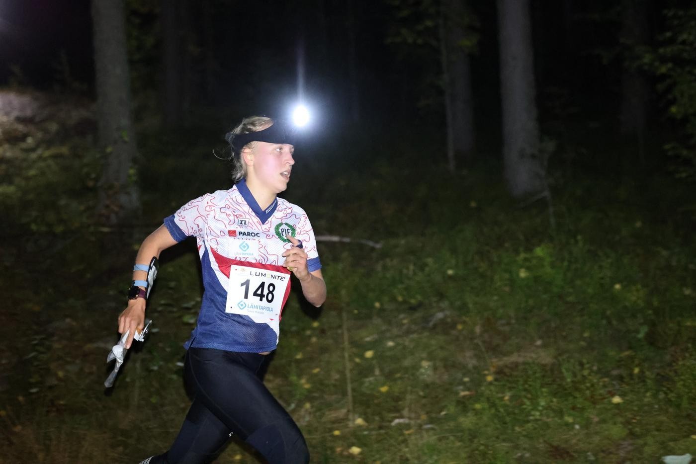 Orienterare springer i mörker med pannlampa på huvudet.