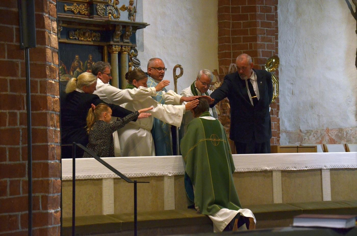 en biskop installerar en kyrkoherde vid altaret