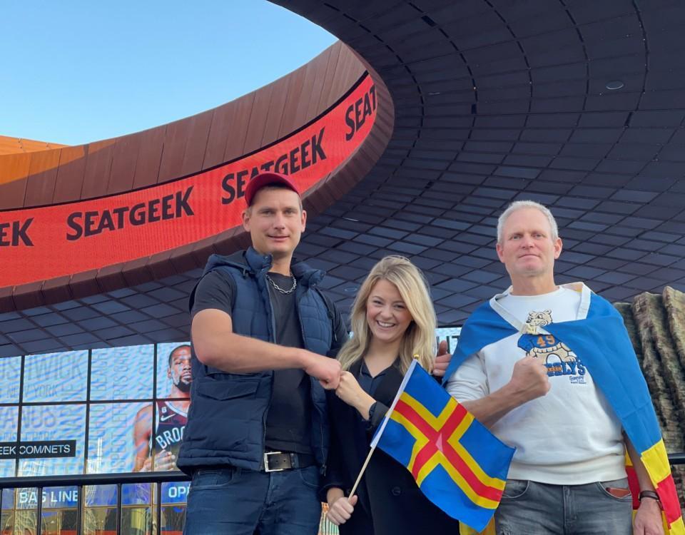 Tre personer med Ålands flagga vid en arena.