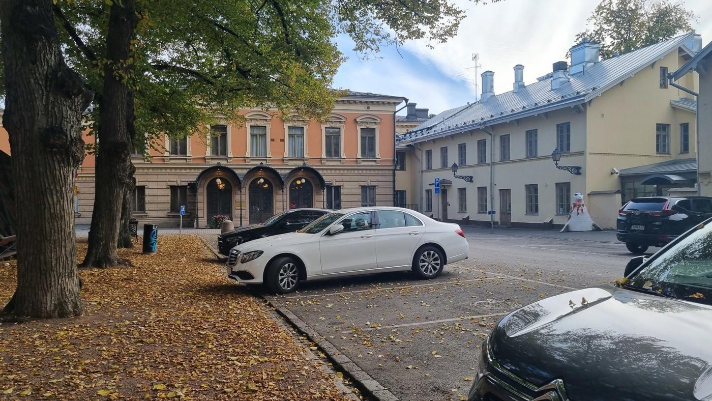 Gamla stadshus med bilar framför, gula löv på marken