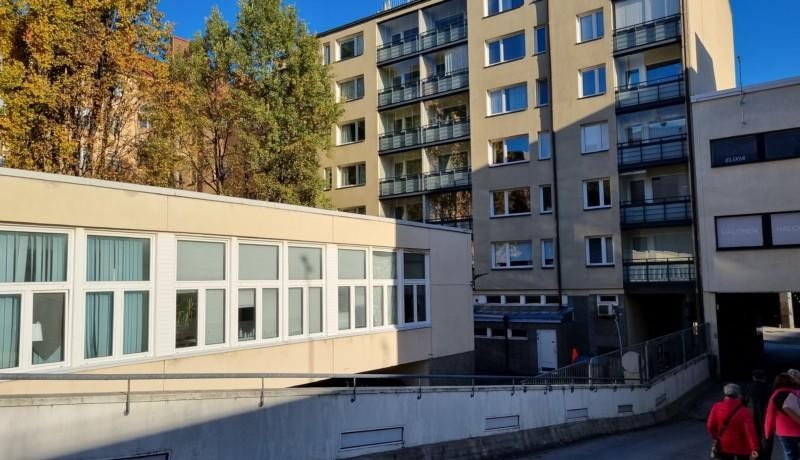 låg byggnad med många fönster och höghus i bakgrunden, höstsol