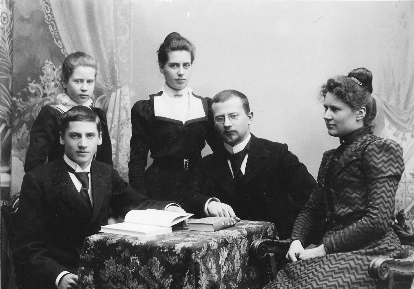 gammalt familjeporträtt med tre kvinnor och två män kring ett bord, svartvitt foto
