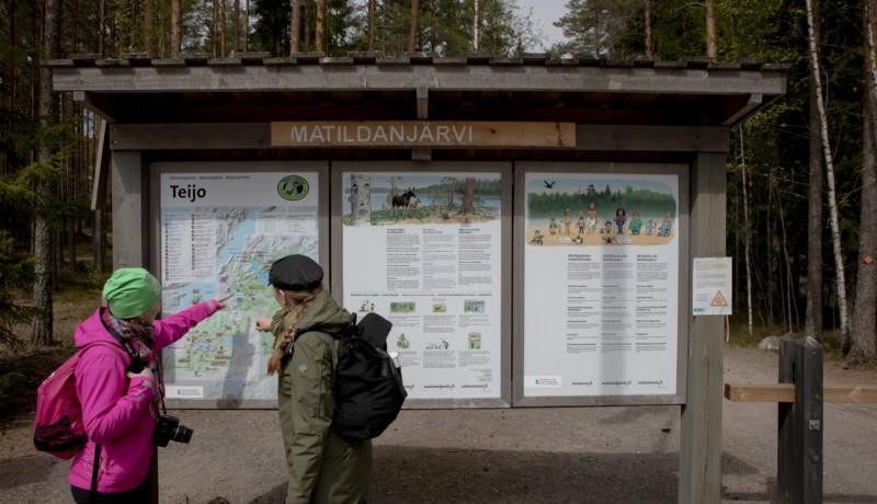 Två personer pekar på en informationsskylt i en skog