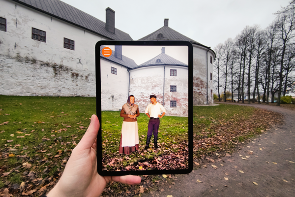 En skärm hålls upp framför slottet och visar folk klädda i 1800-tals kläder.