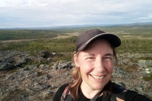 en kvinna med keps ler in i kameran i ödemarksmiljö