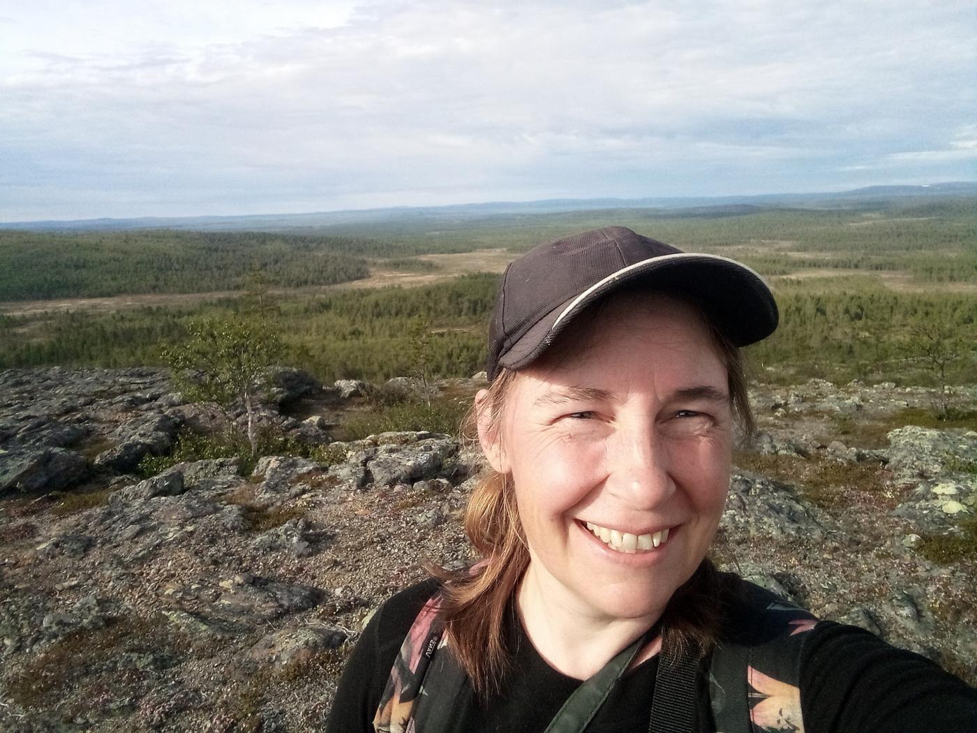 en kvinna med keps ler in i kameran i ödemarksmiljö