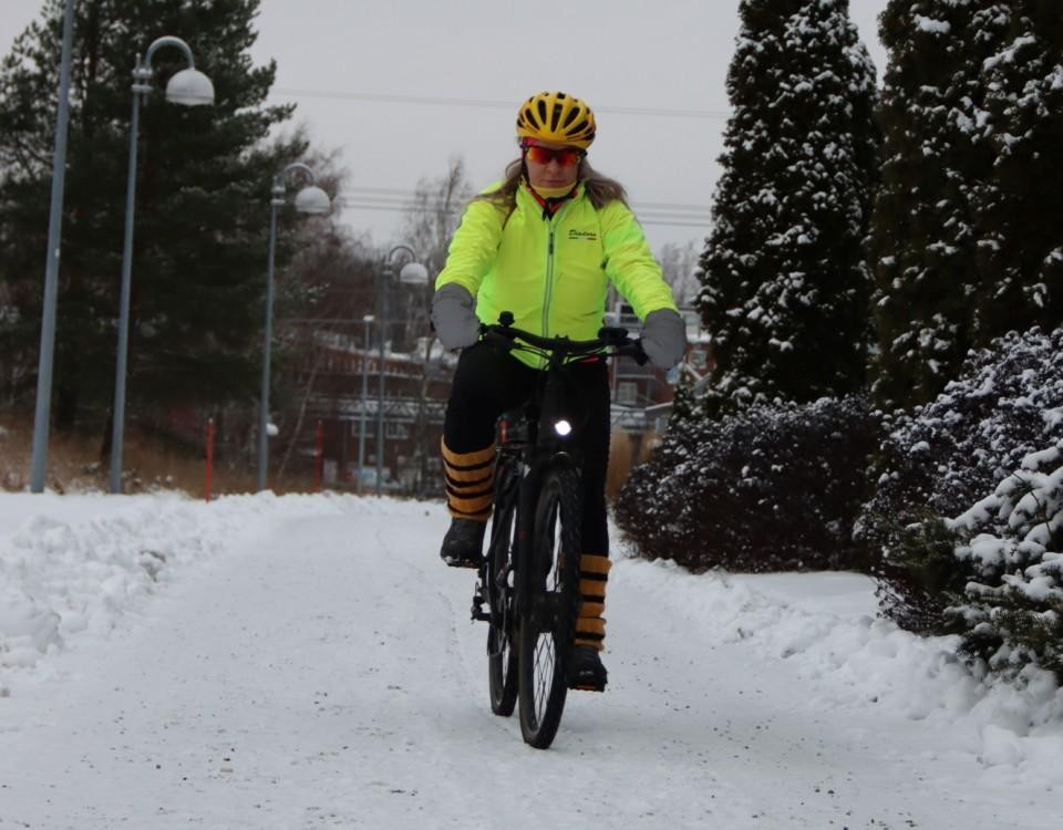 En kvinna som komemr cyklande i ett vintrigt landskap.