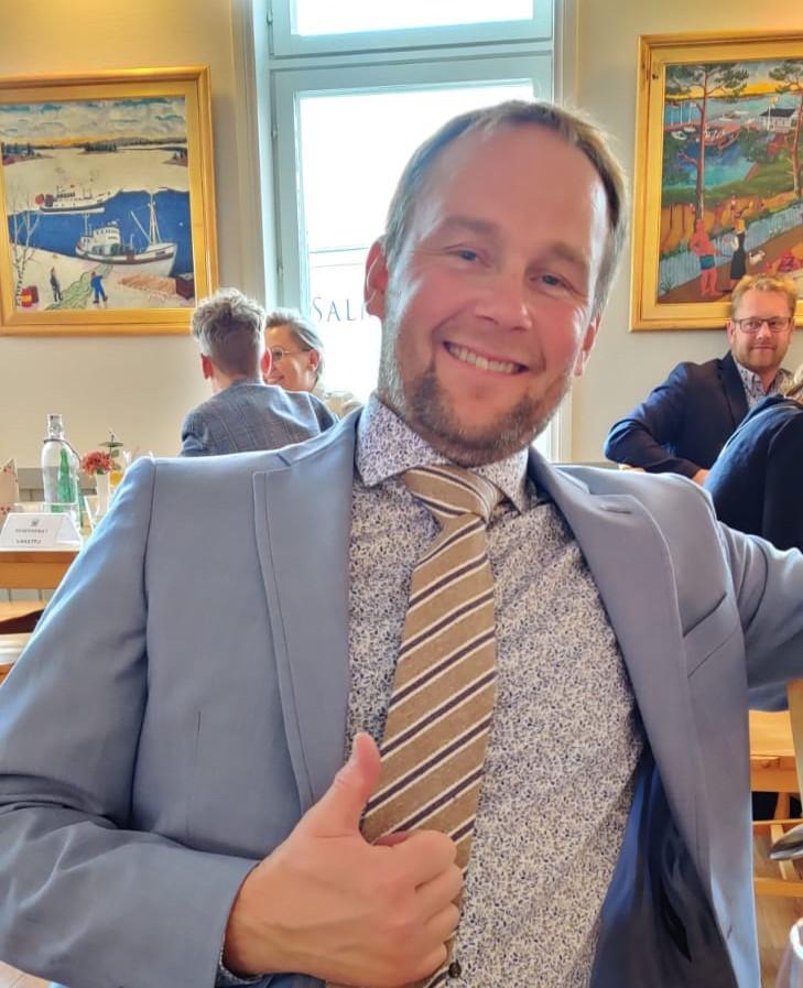 En man i kostym ler och visar tummen upp.