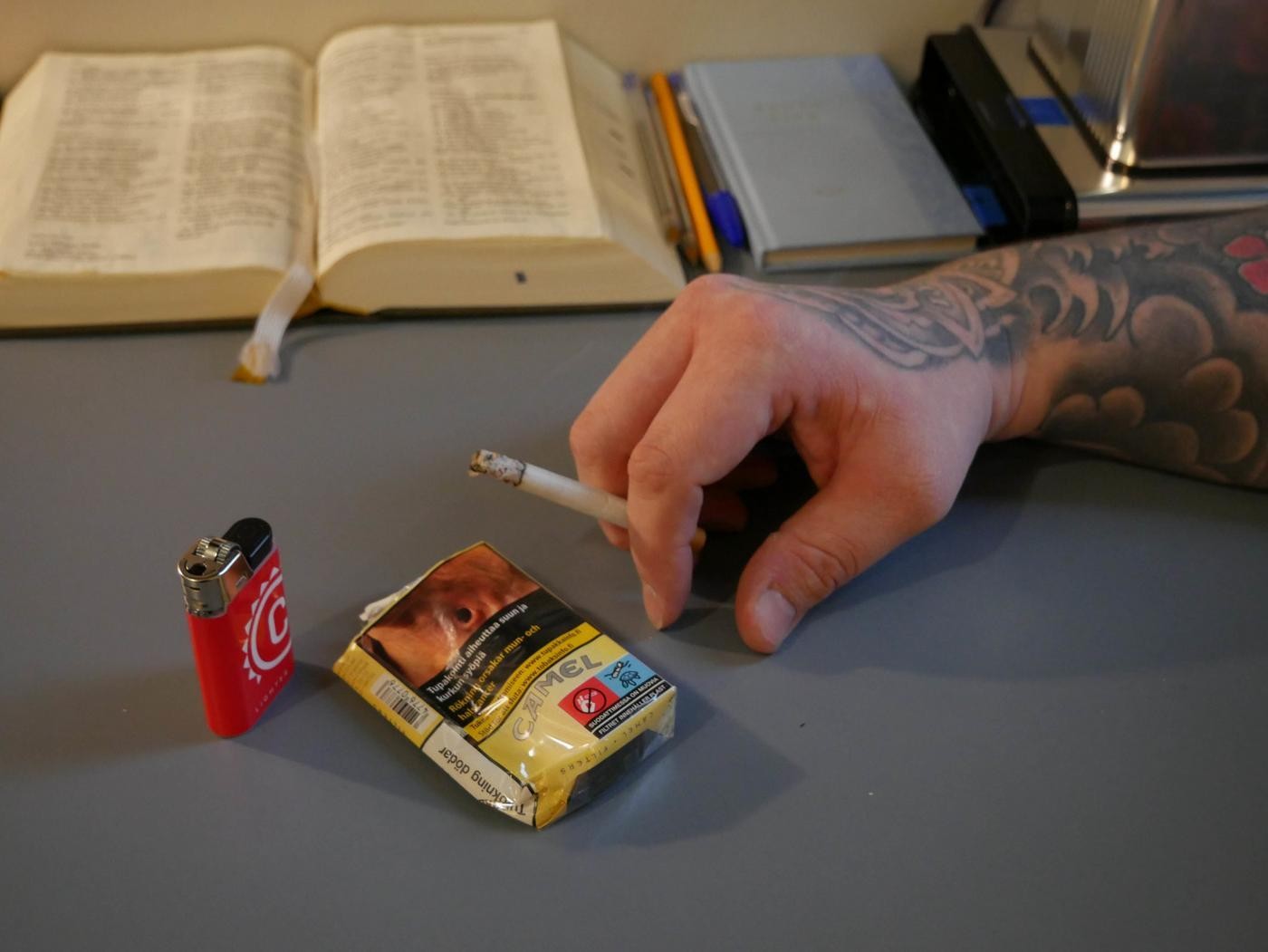 En hand håller i en cigarett ovanför ett ett cigarettpaket