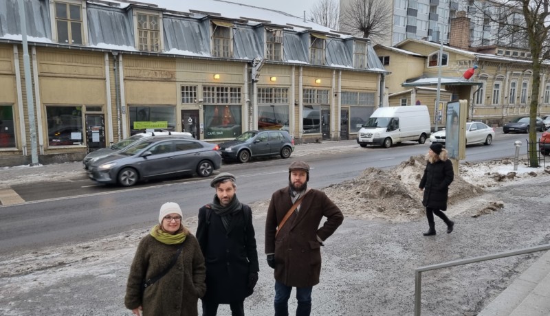 tre person på snöig gata framför gammalt gult trähus