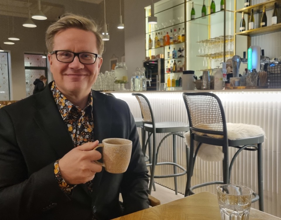 man i kavaj och med glasögon med kaffekopp i handen