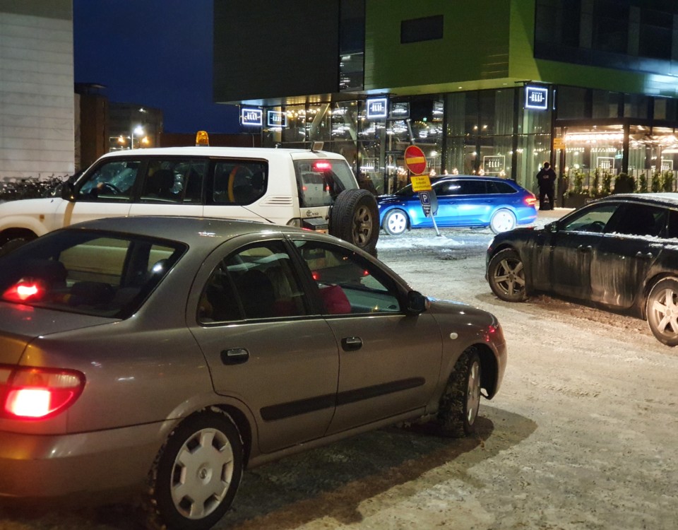 En parkeringsplats i vintermörkret där bilar kör åt olika håll.