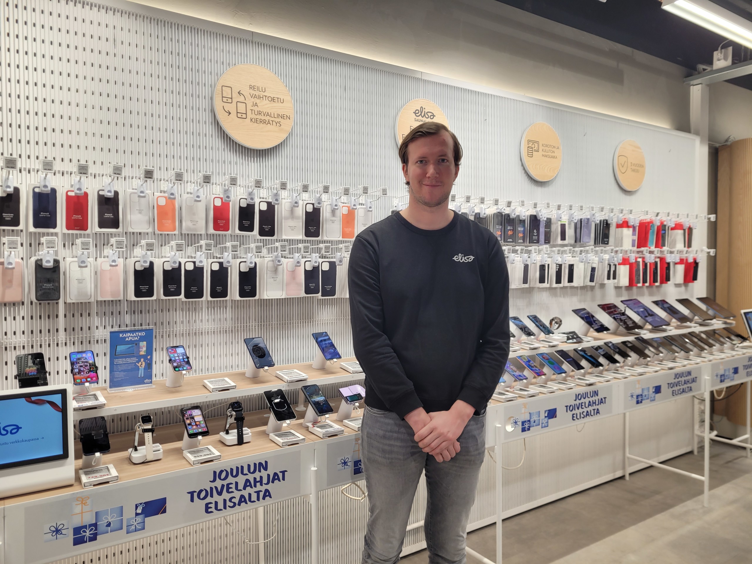 En ung försäljare i en teknikaffär. I bakgrunden syns olika mobilmodeller.