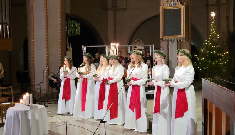 Ett luciafölje står på rad i en kyrka.