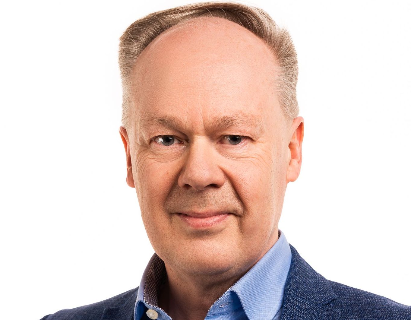 tunnhårig man med skjorta och kavaj tittar mot kameran