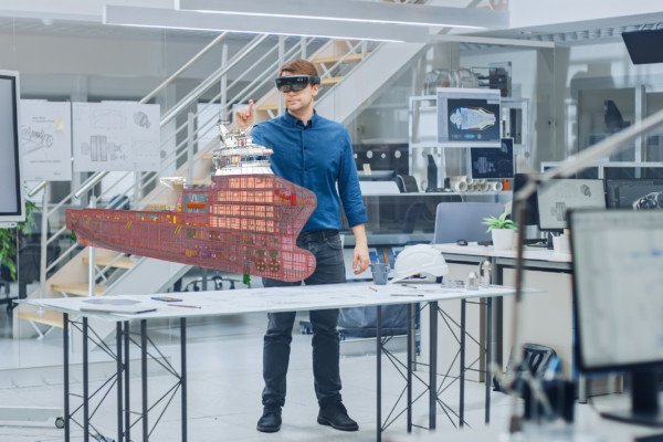 En person med VR-glasögon står framför ett bord med en miniatyrmodell av ett fartyg och håller upp ena handen.