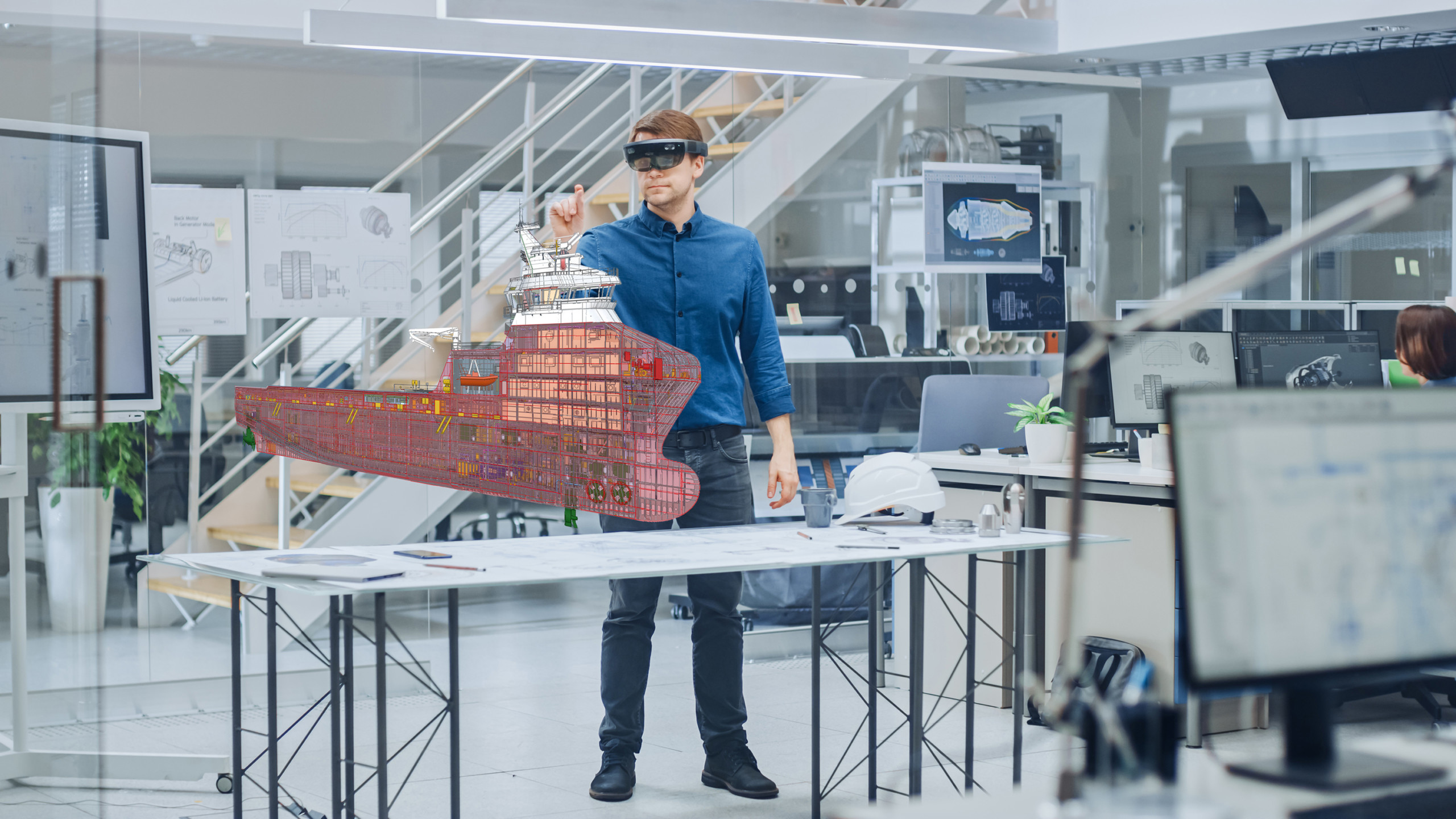 En person med VR-glasögon står framför ett bord med en miniatyrmodell av ett fartyg och håller upp ena handen.