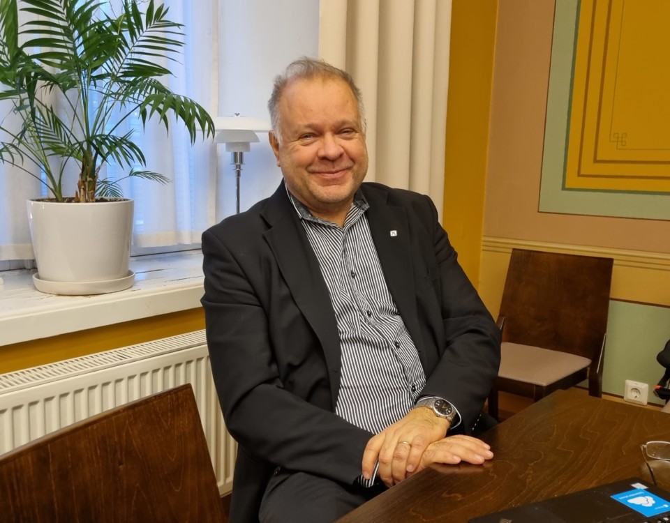 leende man vid skrivbord med palm i kruka i bakgrunden