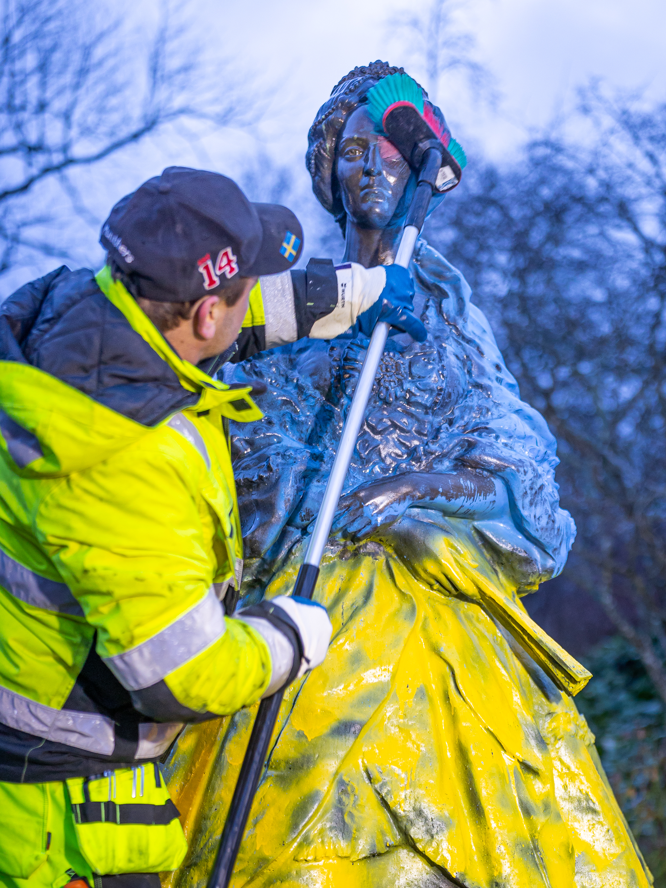 En man i arbetskläder tvättar bort målarfärg på en staty
