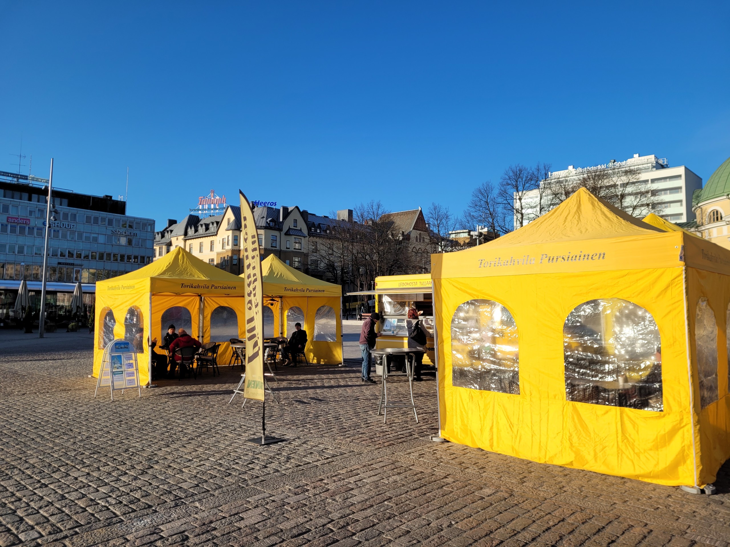 Gula kafétält i solen på ett torg.