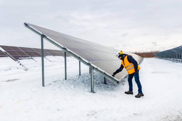 Stor solpanel och en person i reflexväst i vintrigt landskap