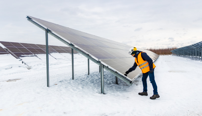 Stor solpanel och en person i reflexväst i vintrigt landskap