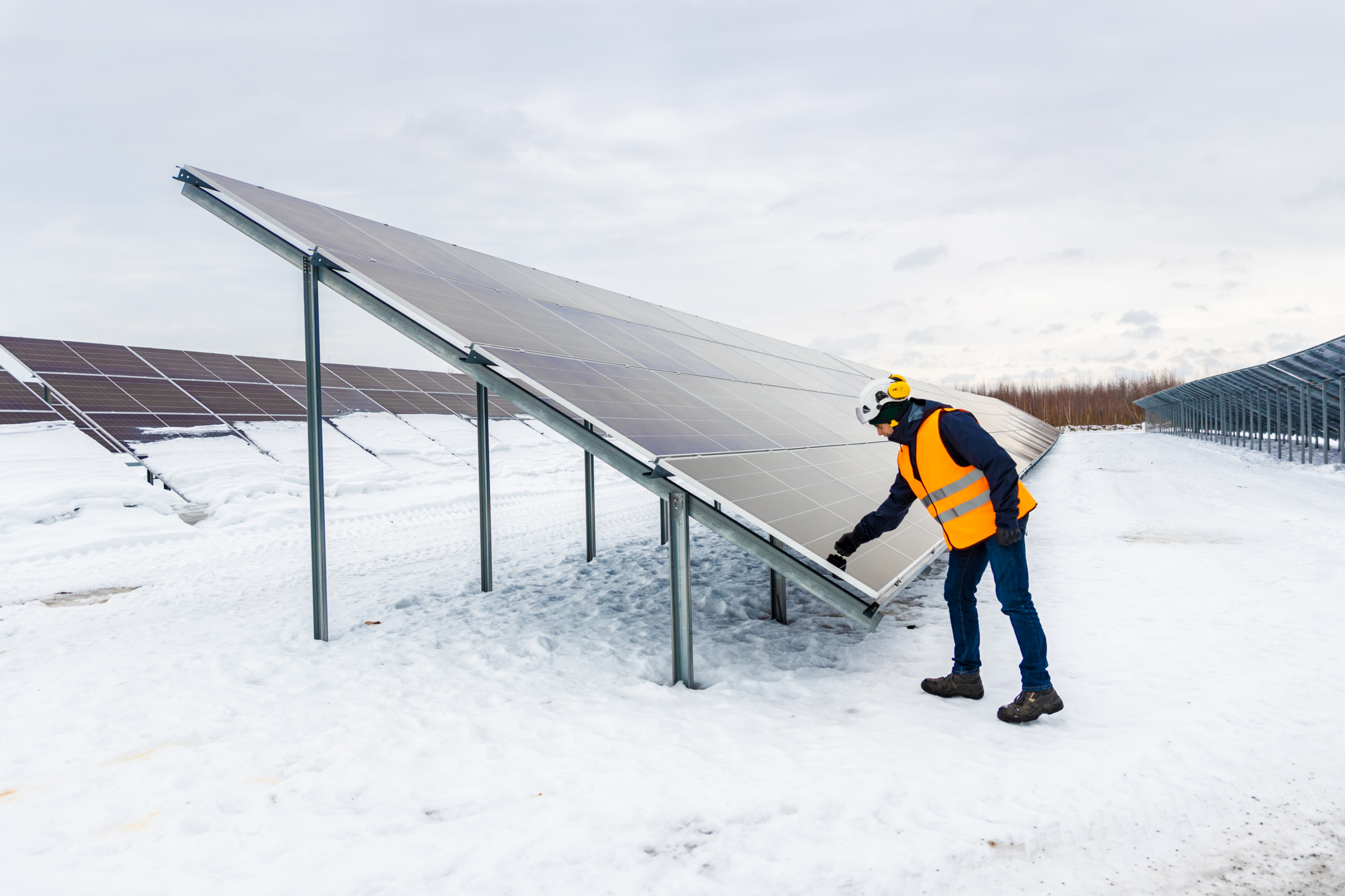 Stor solpanel och en person i reflexväst i vintrigt landskap