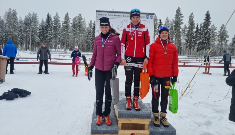 Tre damer i skiddräkter på en prispall.