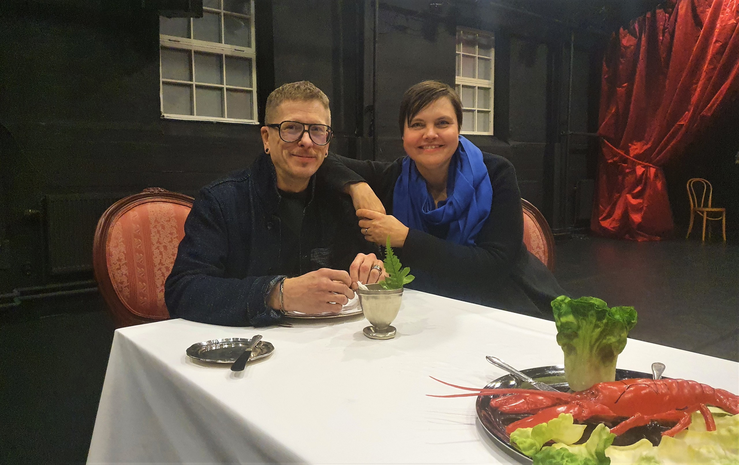 En man och en kvinna vid ett dukat bord på en teaterscen.