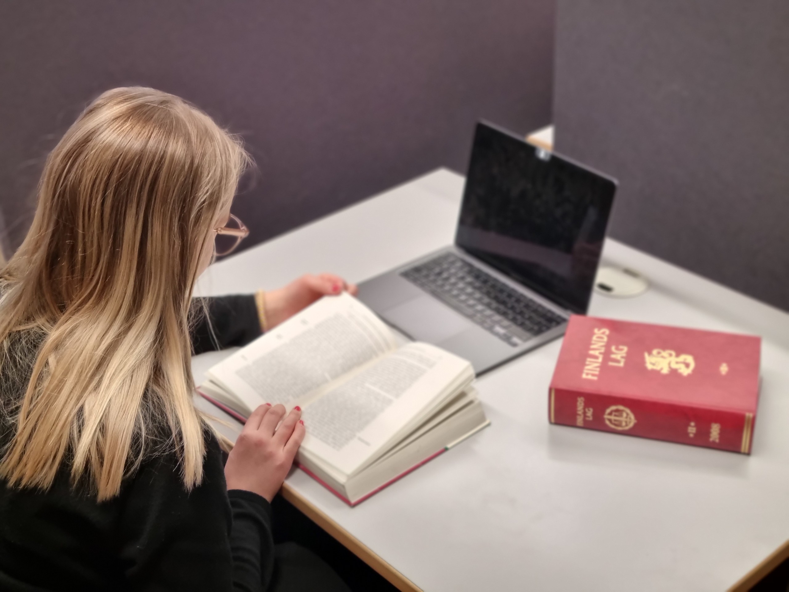 En kvinna som sitter och läser en bok vid en dator
