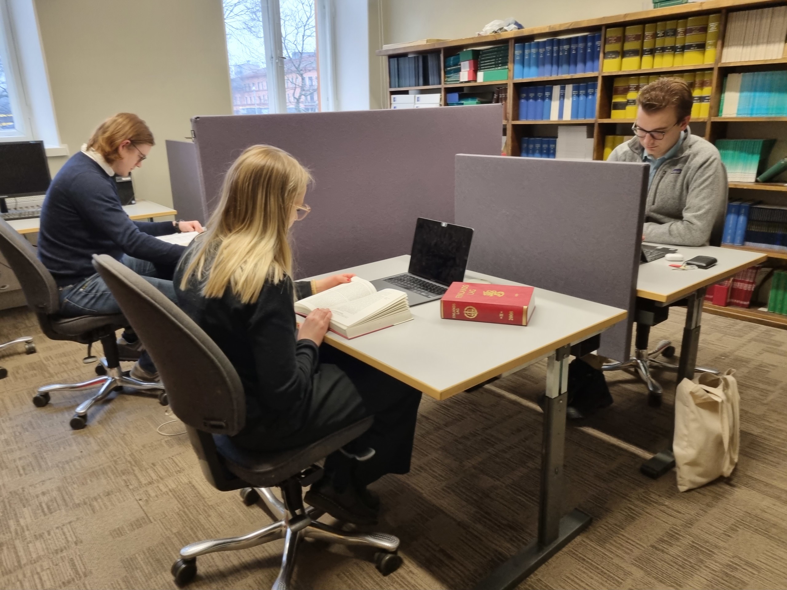 Tre ungdomar som sitter och läser i ett bibliotek