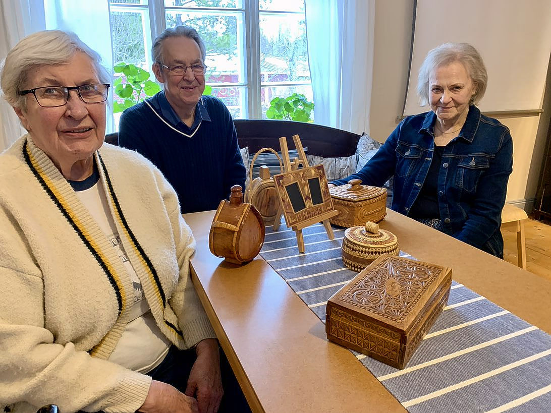 Tre seniorer sitter runt ett bord med gamla föremål