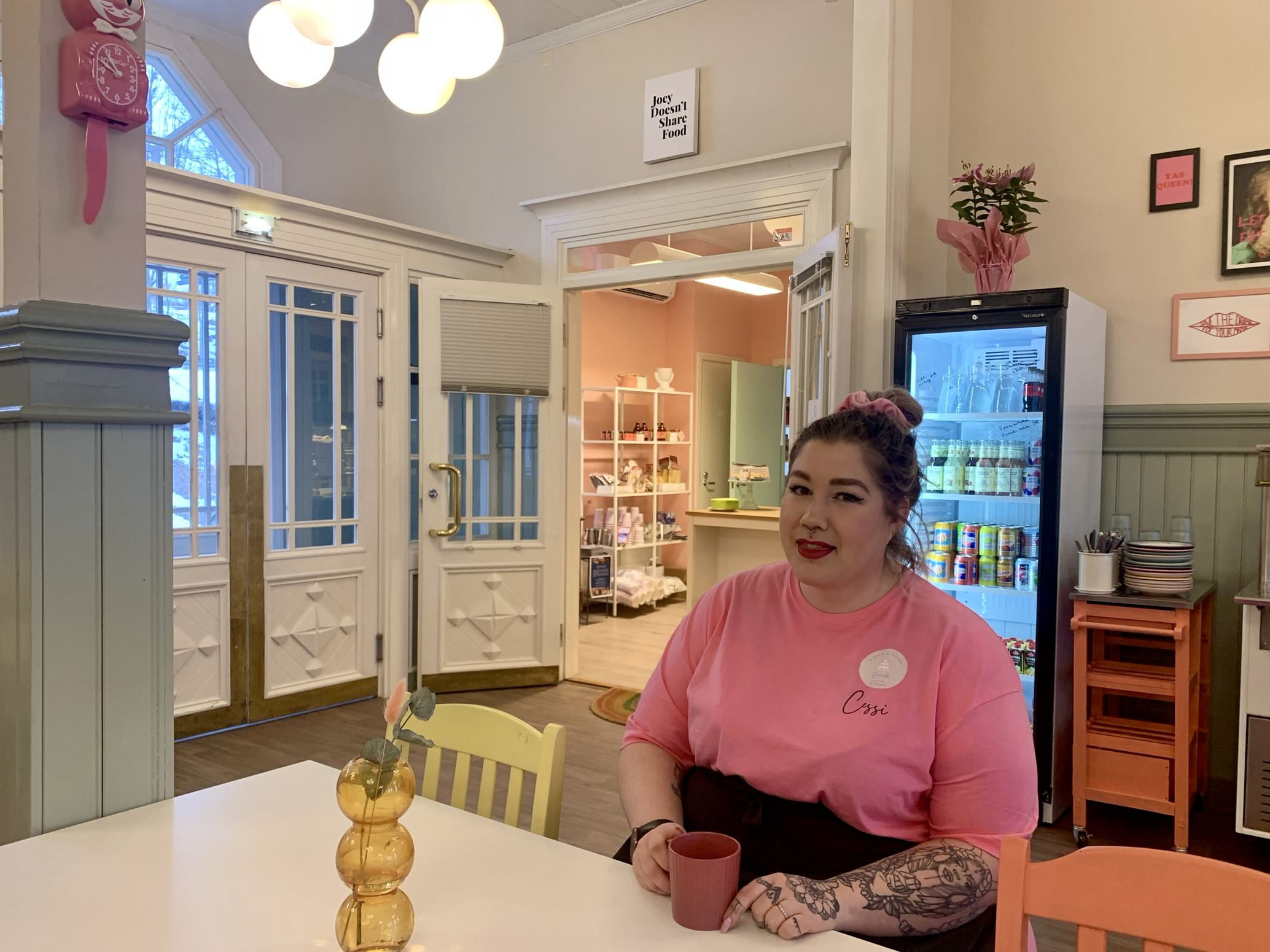 Kvinna i ljusröd tshirt sitter vid ett bord med en kaffekopp