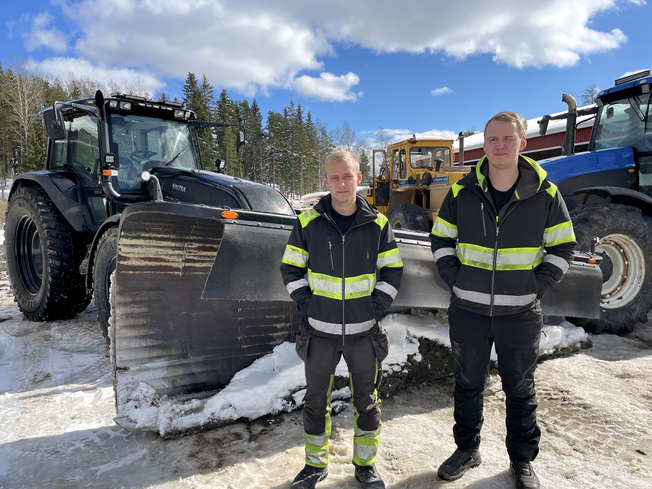 Två unga män i arbetskläder vid en traktor med snöplog.