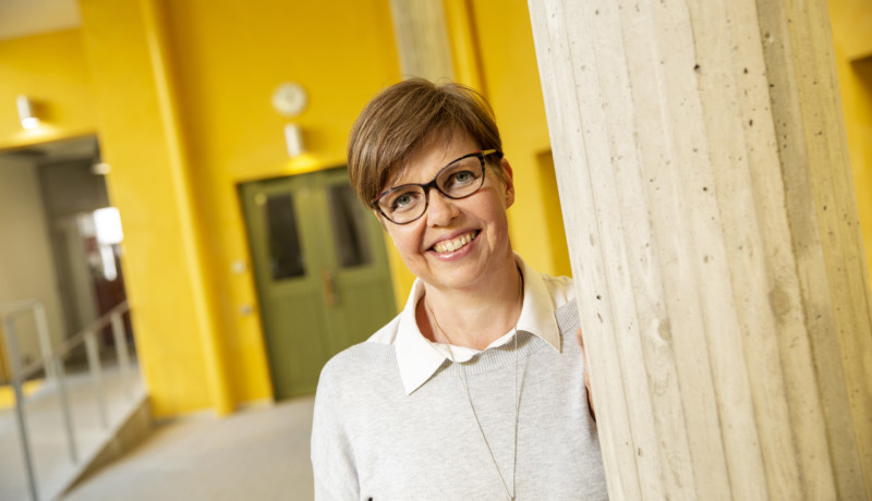 leende kvinna med kort hår och granngul vägg i bakgrunden