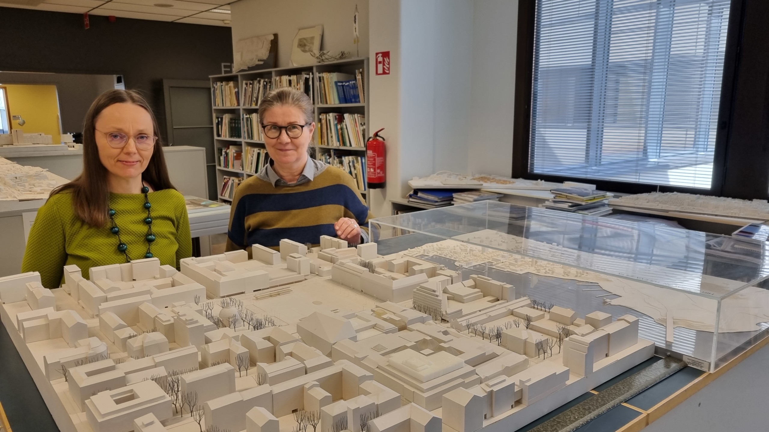 två kvinnor bakom en modell av en stad med vita klossar