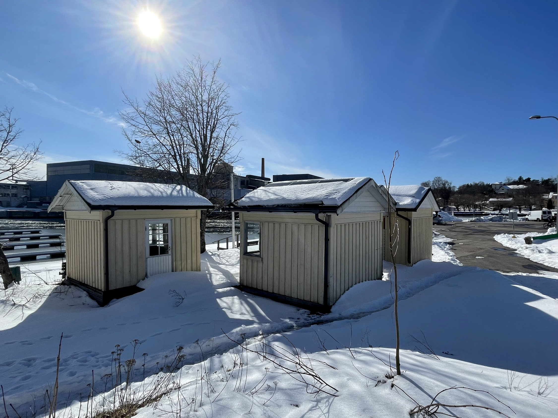 Fyra små bodar i en hamn. Marken är snötäckt. 