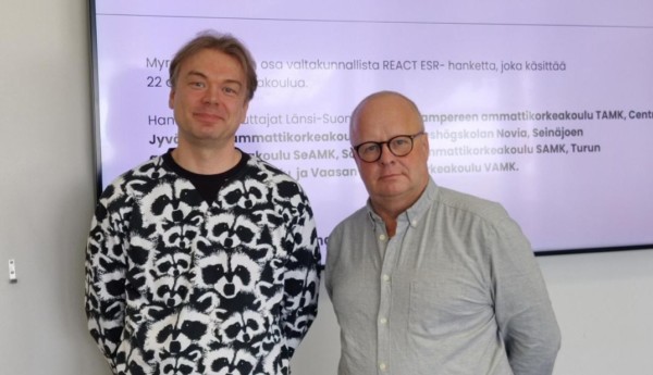 Två män som poserar vid en skärm med text.