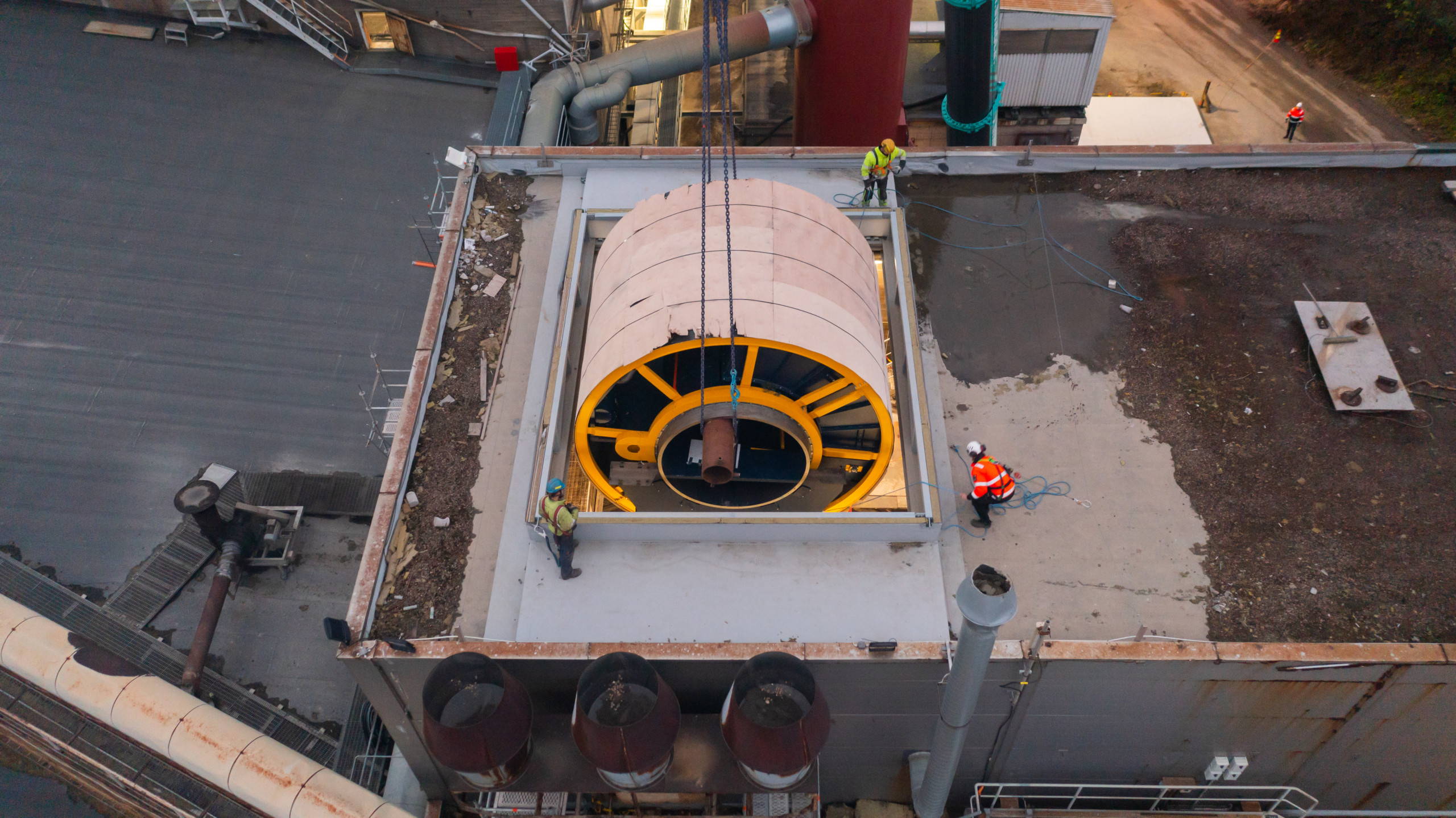 en enorm teknisk maskin lyfts in genom ett hål i taket på en industribyggnad