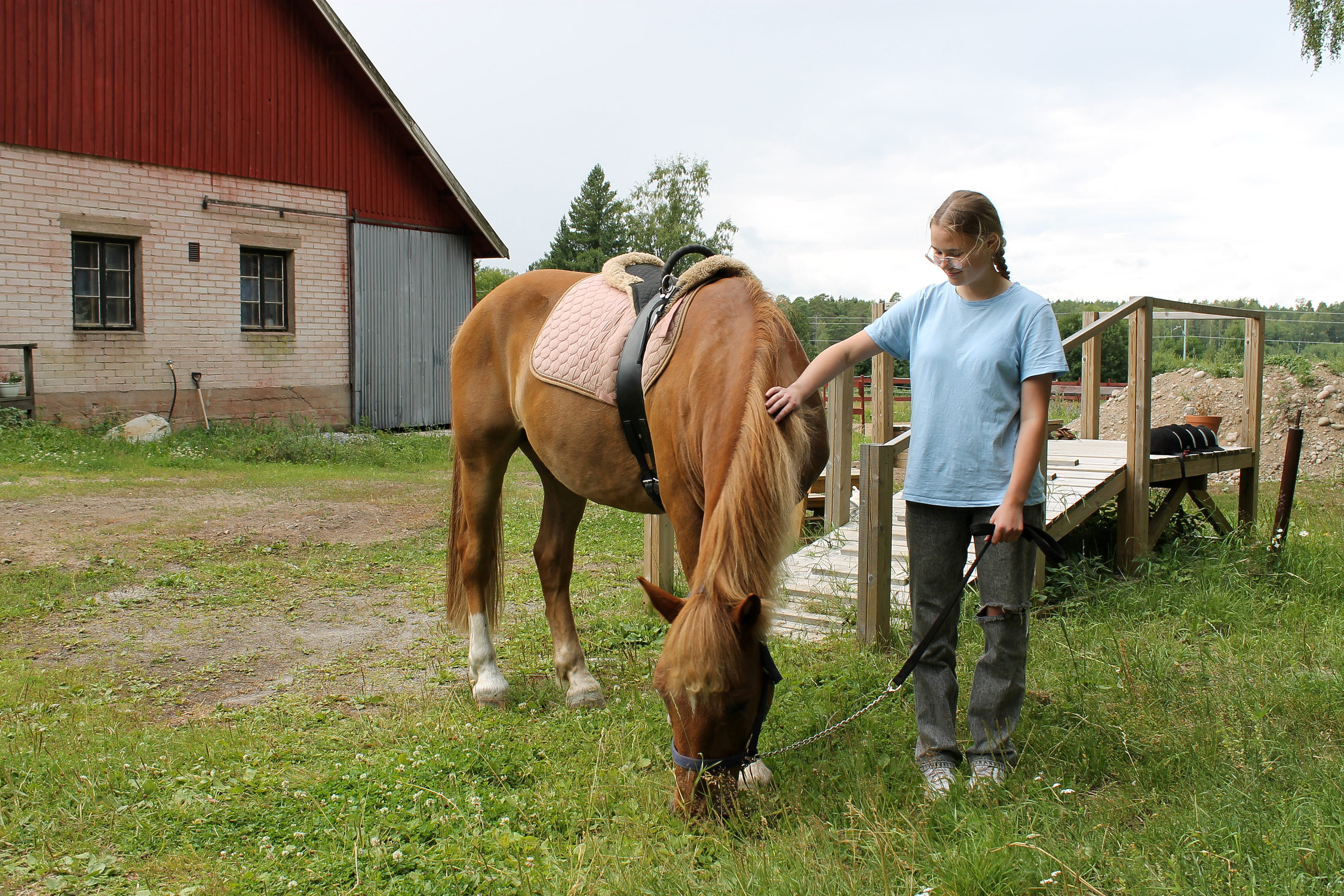 Flicka står bredvid en häst utomhus på en gård.