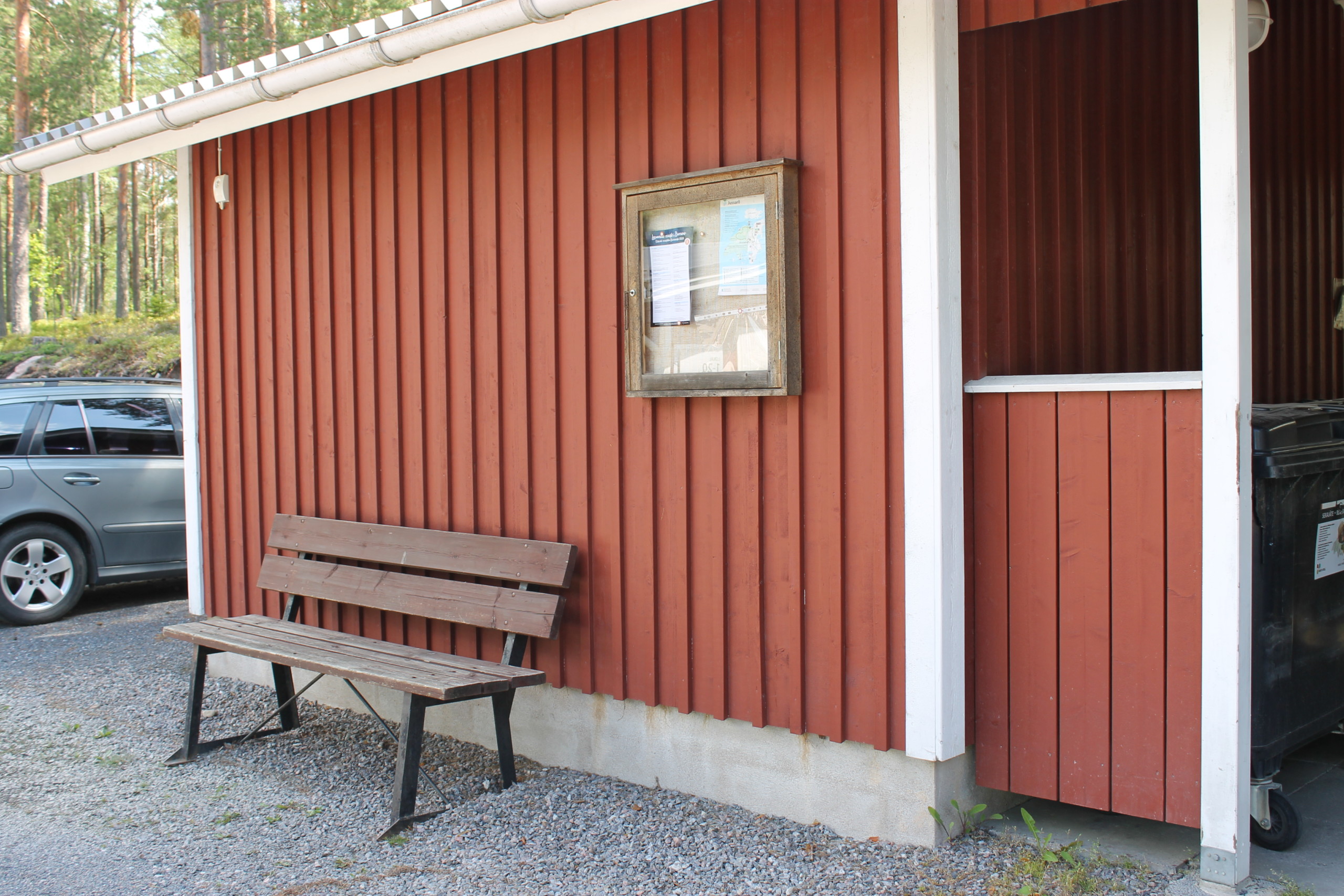 Anslagstavla utomhus på en röd garagebänk, under tavlan finns en bänk.