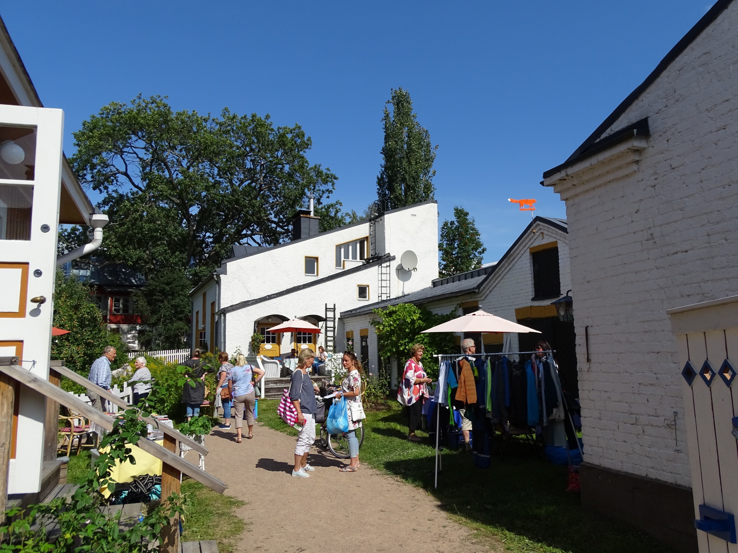En gård i Gamla Stan i Ekenäs en solig sommardag. Människor som står och pratar på en gård som har loppis.