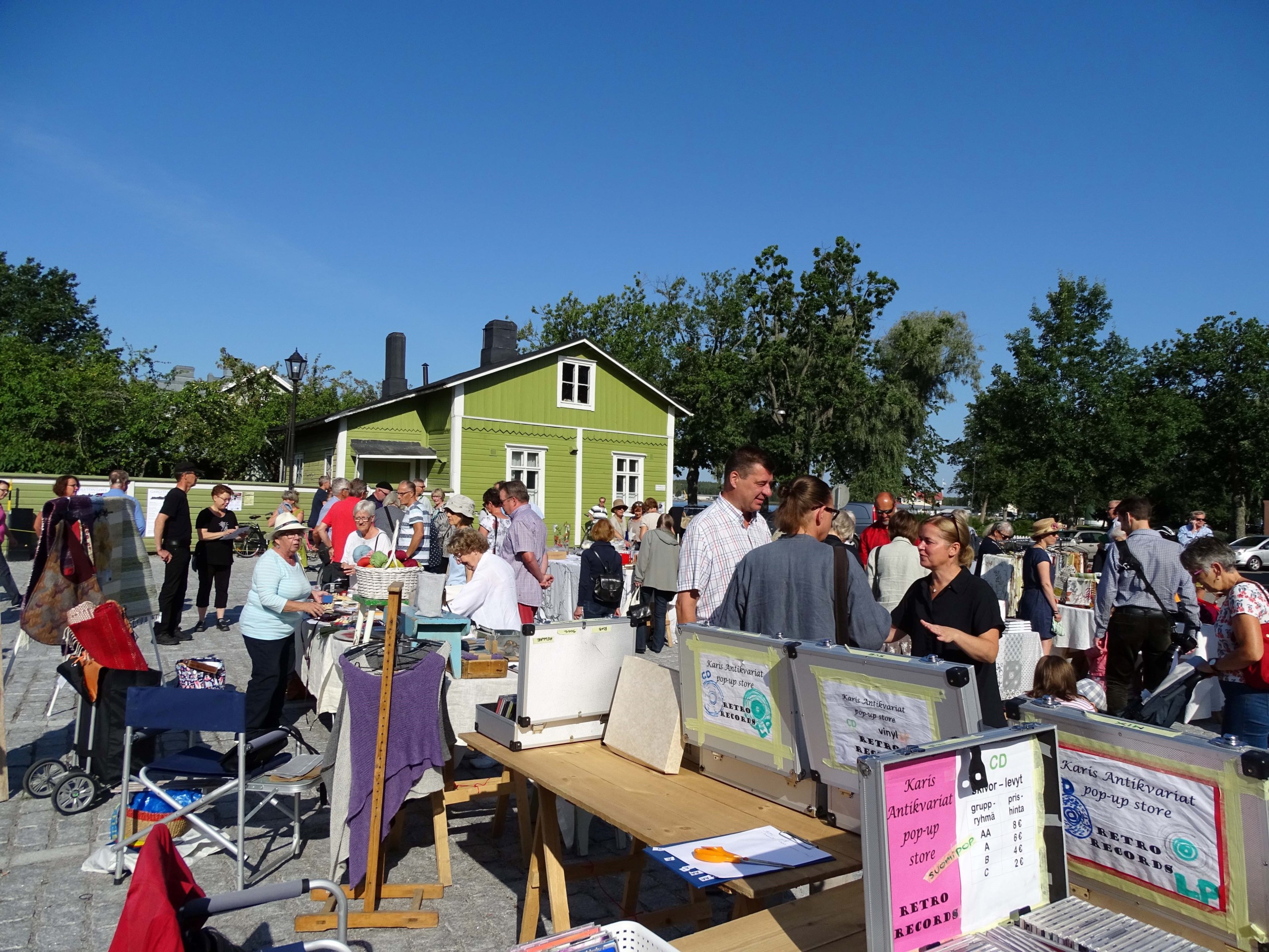 Solig dag på ett torg i Ekenäs med massa människor och loppisbord.