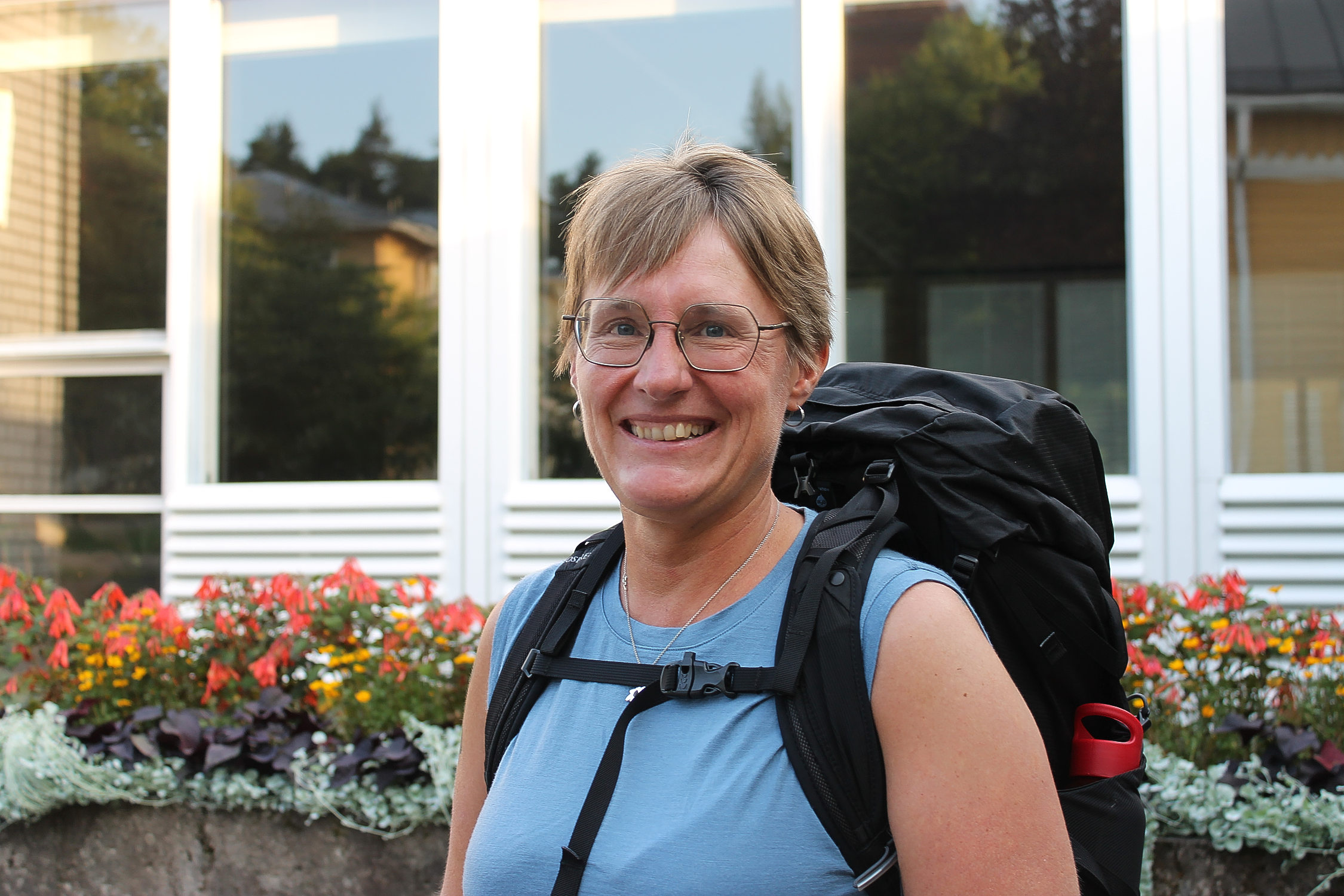 Närbild på en kvinna som ler. Kvinnan har en ryggsäck på ryggen, hon är en av deltagarna i en pilgrimsvandring.