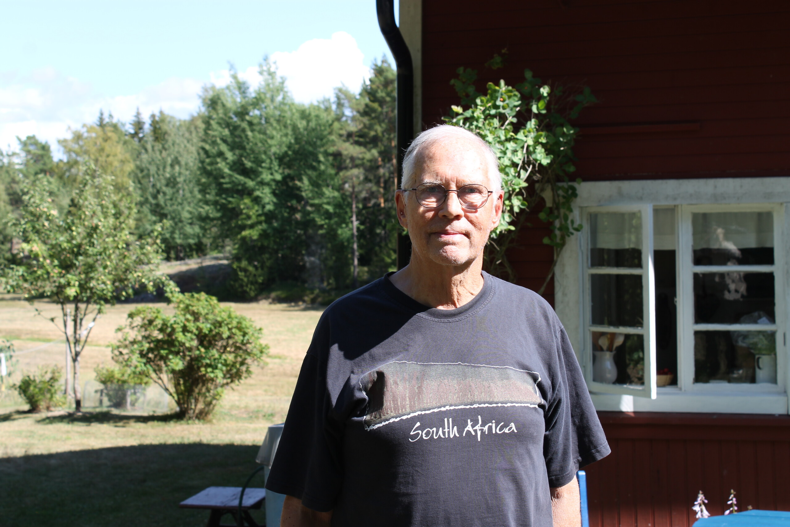 Äldre man med glasögon står framför sitt hus i Bromarv.