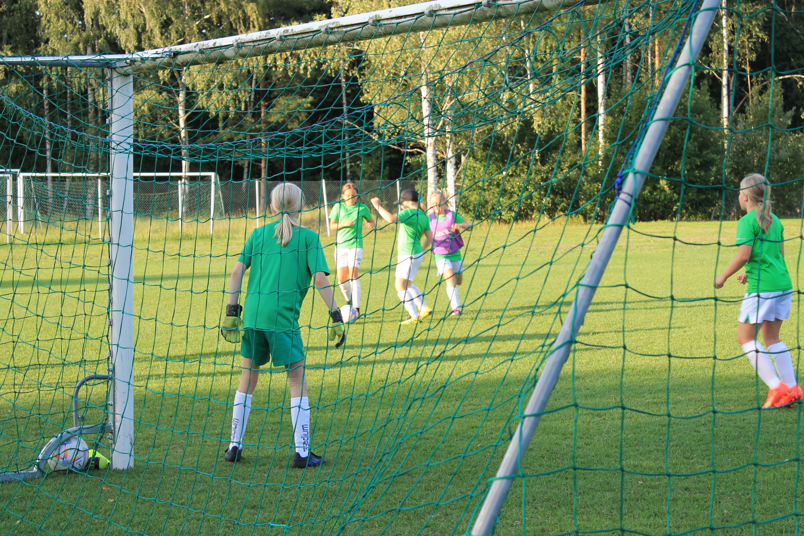 EIF:s fotbollslag med flickor födda 2012 och 2013 håller en träning på en gräsplan i Ekenäs. Bilden är fotograferad bakommålet så man ser målvaktens rygg och några spelare som försöker ta bollen.