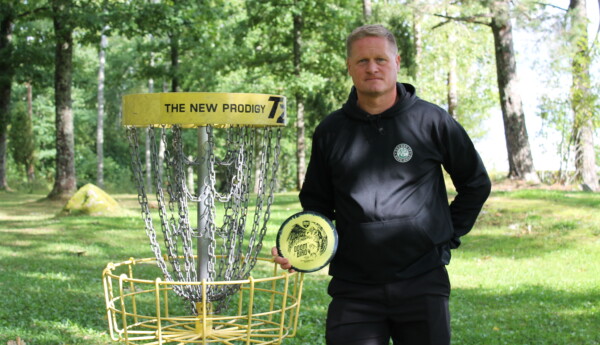 Man står bredvid en frisbeegolfkorg med en disc i handen.