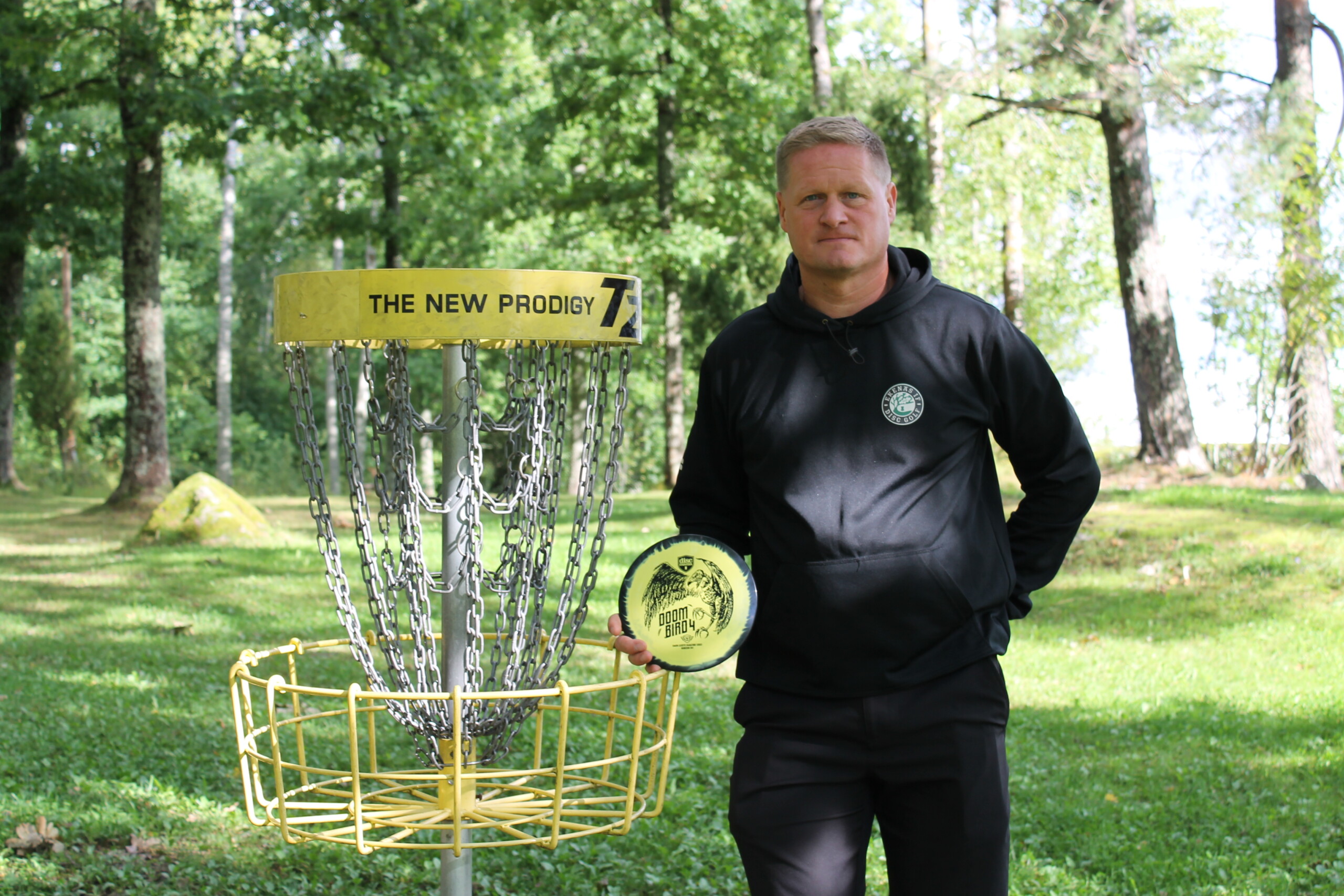 Man står bredvid en frisbeegolfkorg med en disc i handen.