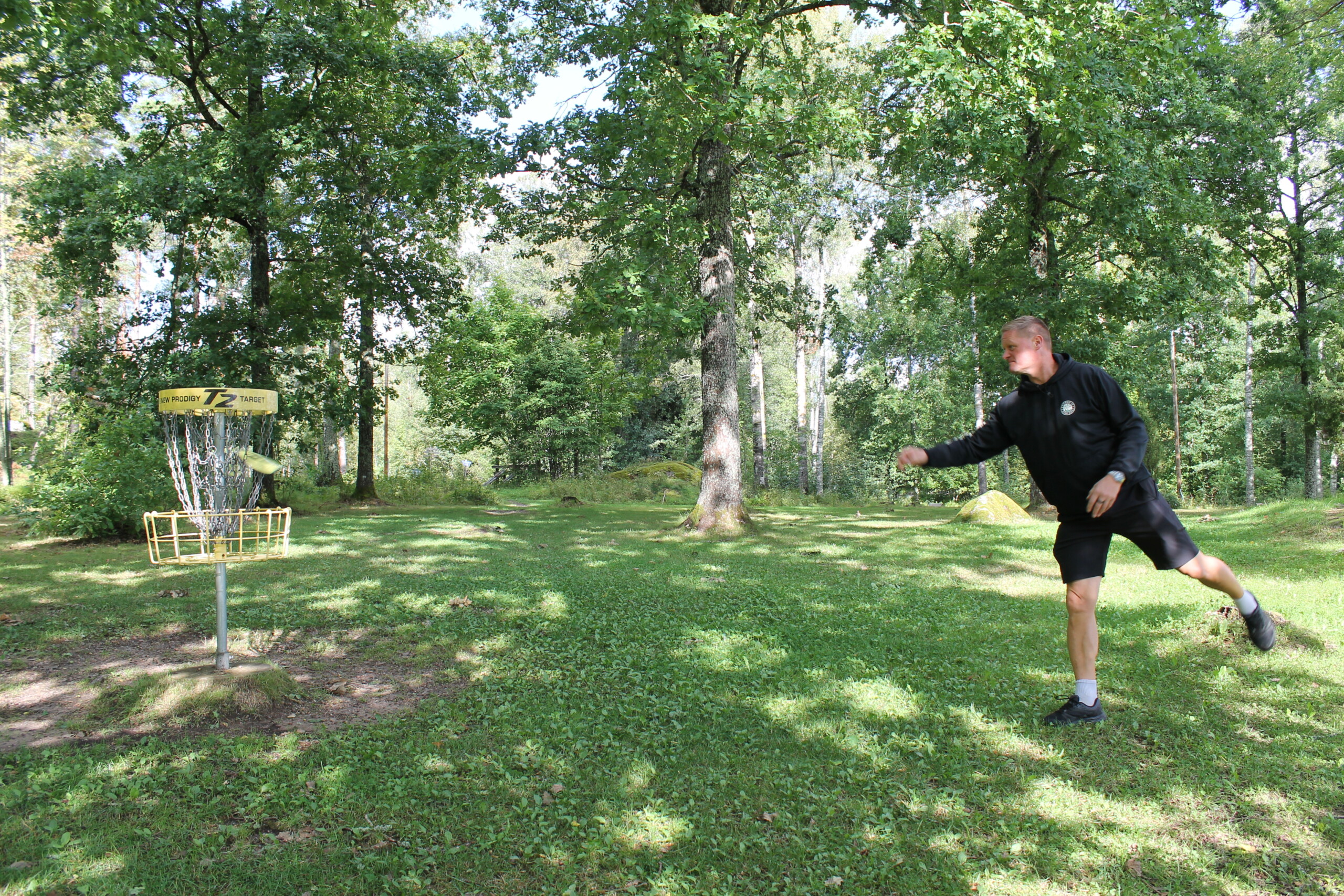 Man kastar en frisbee mot en firsbeegolfkorg i Västerby, Ekenäs.
